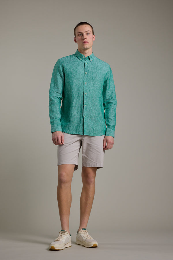 A person stands against a plain background, wearing a Barkers Dorset Linen Shirt in teal, light beige shorts, and white sneakers. They have a neutral expression and relaxed arms at their sides.