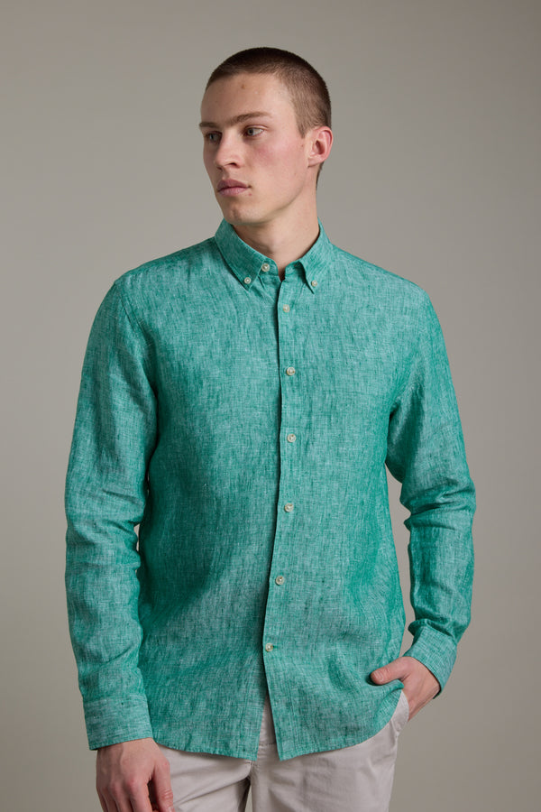 A young man with short hair wears the Barkers Dorset Linen Shirt in green, tailored fit, paired with light pants. He stands against a plain background, looking slightly to the side with one hand in his pocket.