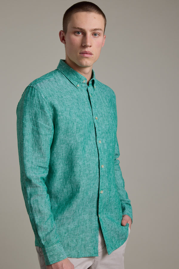 A young man with short hair wears the Barkers Dorset Linen Shirt in teal, paired with light pants. He stands against a plain background, one hand in his pocket, looking at the camera.