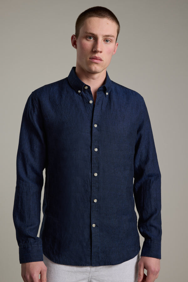 A young man with short hair wears the Barkers Dorset Linen Shirt, a dark blue tailored fit style, paired with light pants. He stands against a plain light gray background, looking at the camera with a neutral expression.