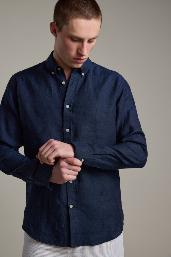 A person fastens the cuff of a Dorset Linen Shirt by Barkers in dark blue tailored fit, looking down against a plain, neutral background.