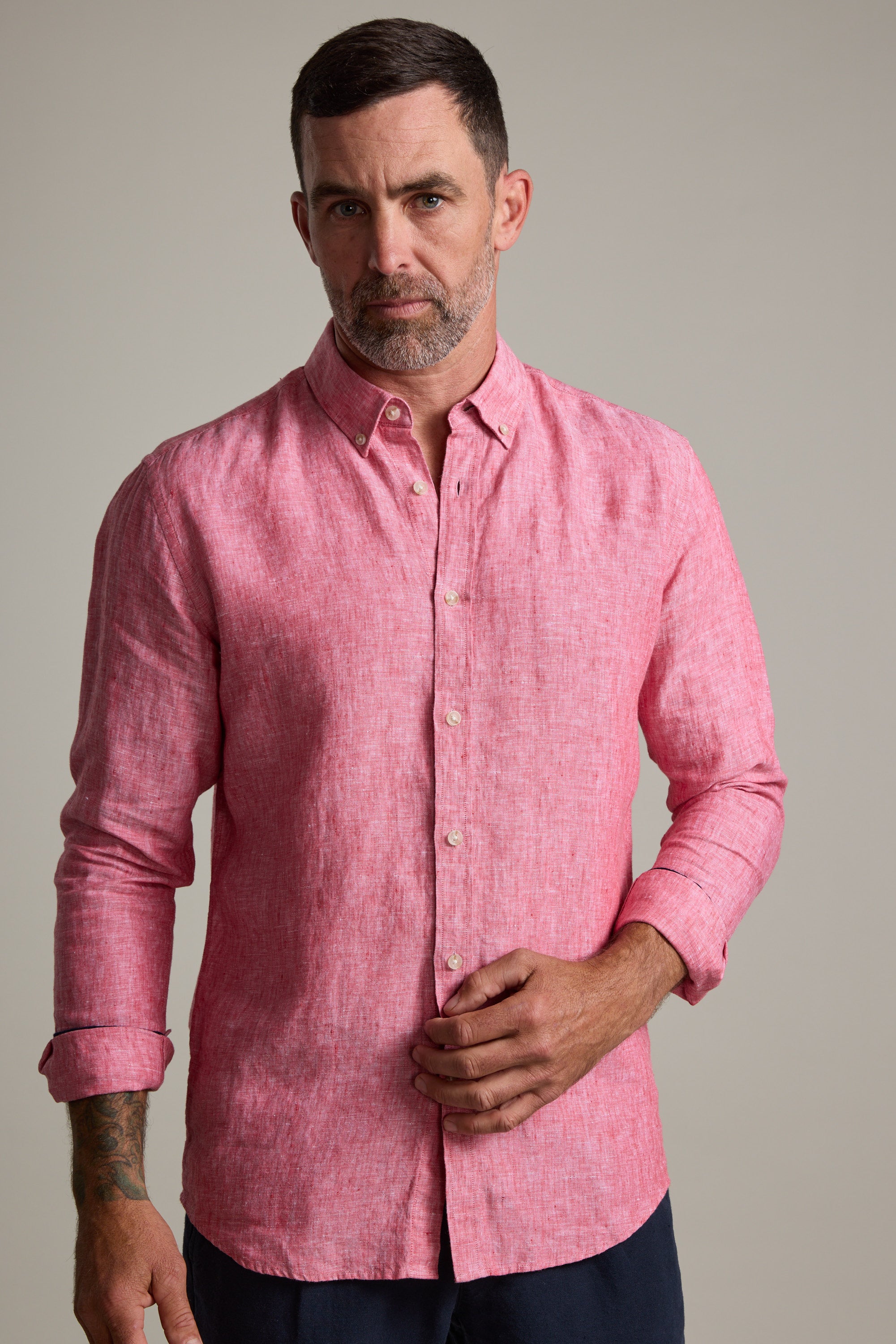 A man with short dark hair and a beard wears the Barkers Dorset Linen Shirt in pink, tailored fit with long sleeves rolled up, standing against a plain light background.