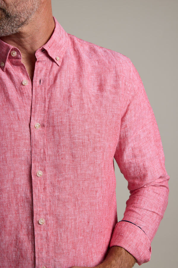 A man wears the Barkers Dorset Linen Shirt, a light red tailored-fit French linen style with rolled-up sleeves, shown from shoulders to waist against a plain background. His face is partially out of frame.