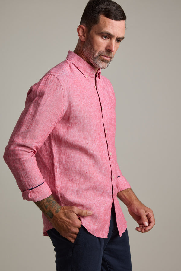 A man with short dark hair and a beard wears the Barkers Dorset Linen Shirt in pink and dark pants, standing with one hand in his pocket against a plain background.