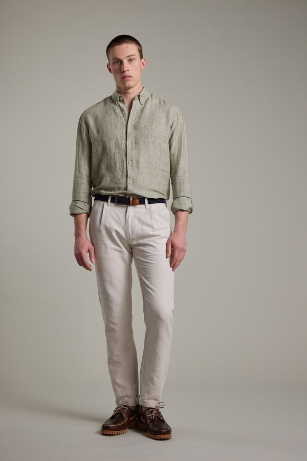 A young man with short hair stands against a plain background, wearing the Barkers Dorset Linen Shirt in light green with rolled sleeves, beige pants, a black belt, and brown shoes. The breathable fabric and tailored fit enhance his refined look.