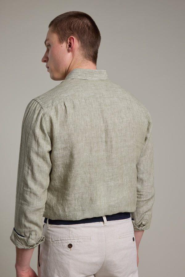 A man with short brown hair is seen from the back, wearing Barkers’ Dorset Linen Shirt in light green and light beige pants with a black belt. The tailored fit and breathable linen fabric stand out against the plain background.