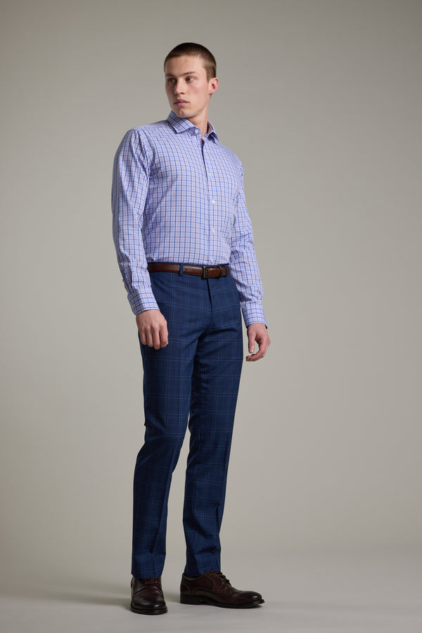A man stands against a plain background wearing the Barkers Denton Check Business Shirt, blue plaid dress pants, a brown belt, and brown dress shoes. He looks slightly left with a neutral expression. The tailored cotton shirt completes his polished look.