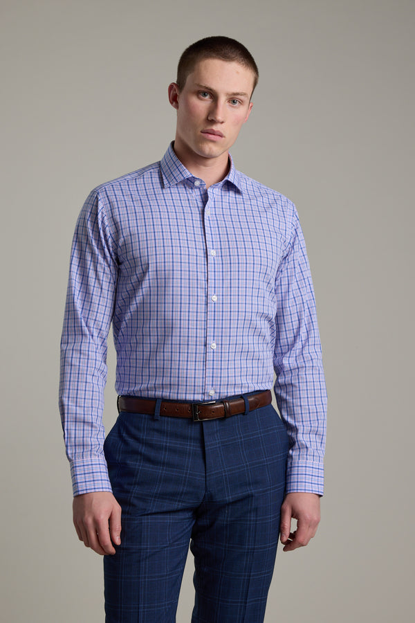 A young man with short hair wears the Barkers Denton Check Business Shirt, tucked into blue plaid pants with a brown belt. He stands against a plain light gray background, looking directly at the camera.
