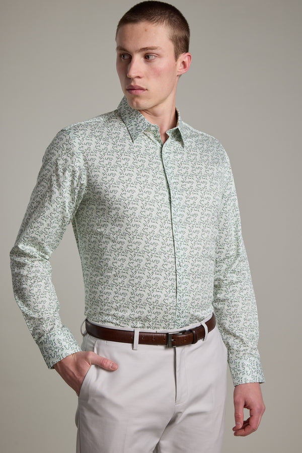 A young man wears the Barkers Ambrose Print Shirt in light green, made from responsibly sourced cotton, paired with beige pants and a brown belt, standing with one hand in his pocket and looking to his left against a plain background.
