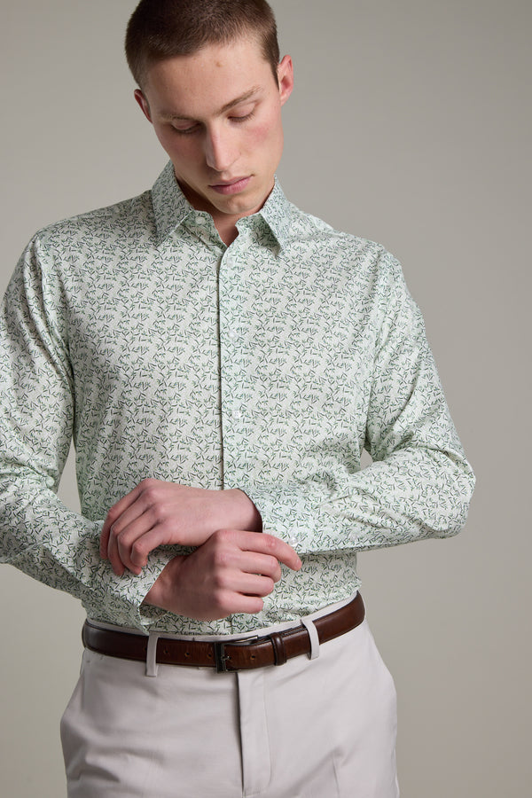 A man in a Barkers Ambrose Print Shirt and beige trousers with a brown belt adjusts his shirt cuff while looking down against a plain background.
