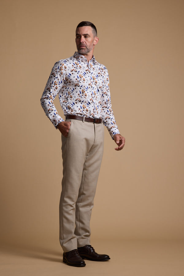 A man stands against a beige background wearing the Barkers Milo Print Shirt, beige trousers, a brown belt, and dark brown dress shoes. He looks to the side with one hand in his pocket, highlighting the shirt’s tailored fit.