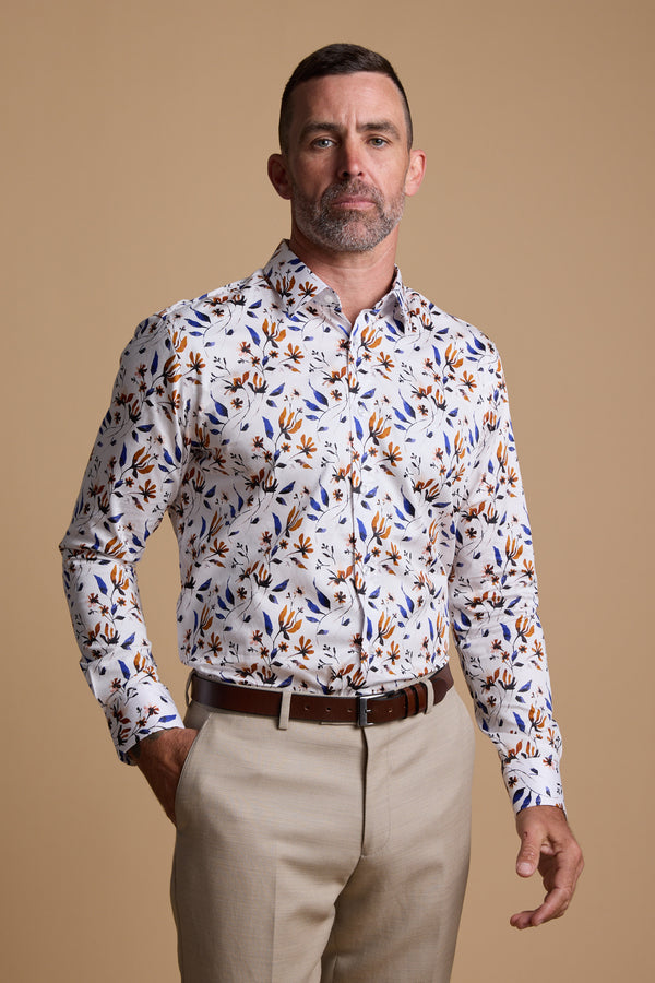 A man with short brown hair and a beard wears the Barkers Milo Print Shirt, a tailored floral design, paired with light beige trousers, standing against a plain tan background.