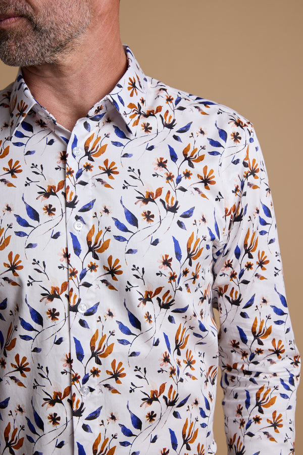 A man wearing the Barkers Milo Print Shirt—tailored fit with a floral pattern in orange, brown, and blue—stands against a beige background, showing only his lower face and upper torso.