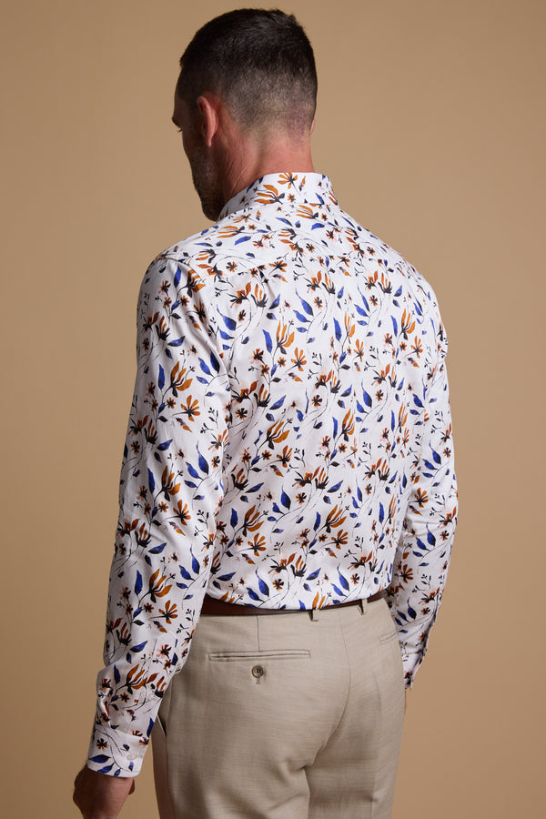 A man stands with his back to the camera against a plain beige background, wearing Barkers' Milo Print Shirt—a white long-sleeve shirt with a blue and brown leaf pattern—paired with beige pants.