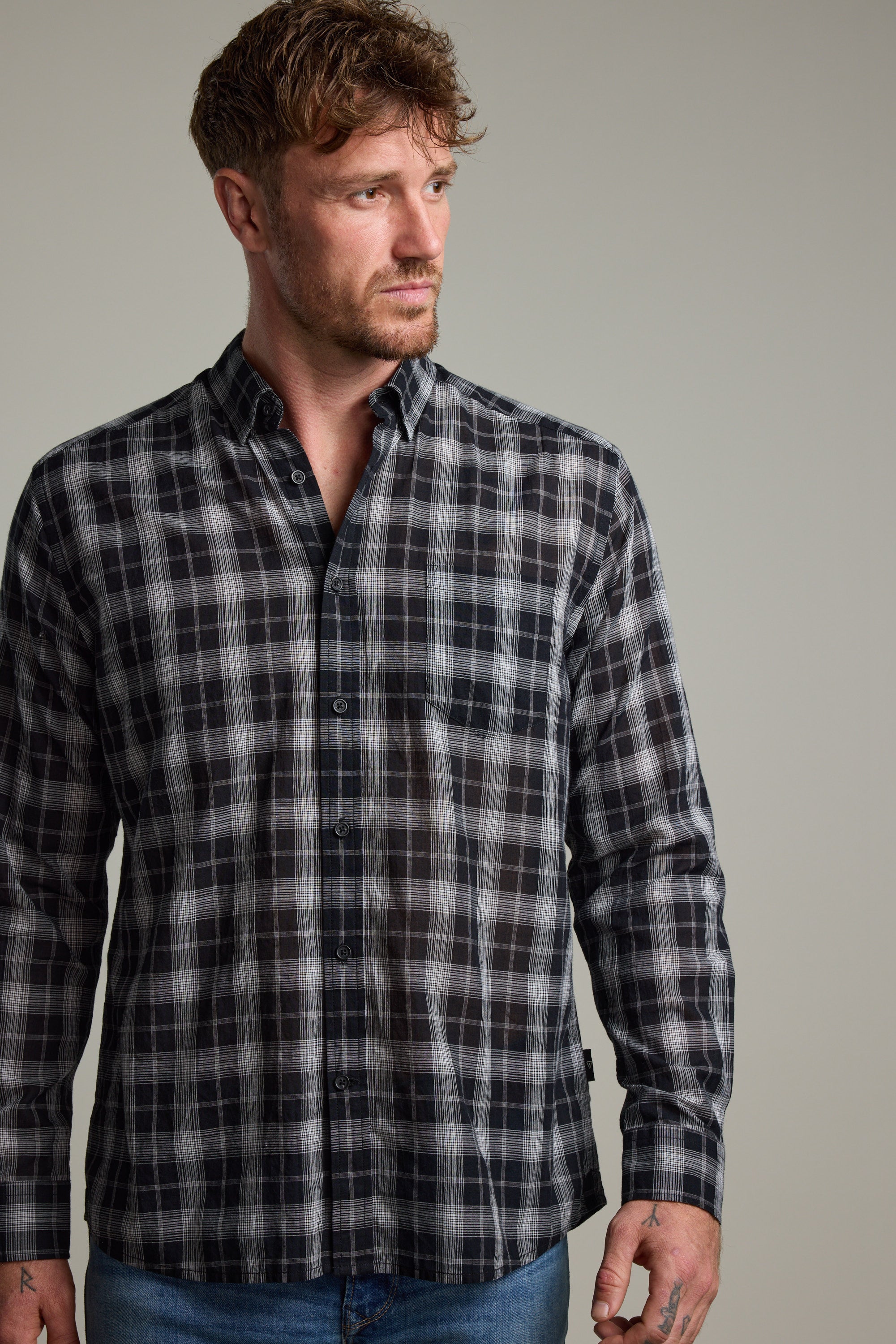A man with short brown hair and a beard wears the Barkers Carter Check Shirt in black, white, and gray with blue jeans, looking to the side against a neutral background.
