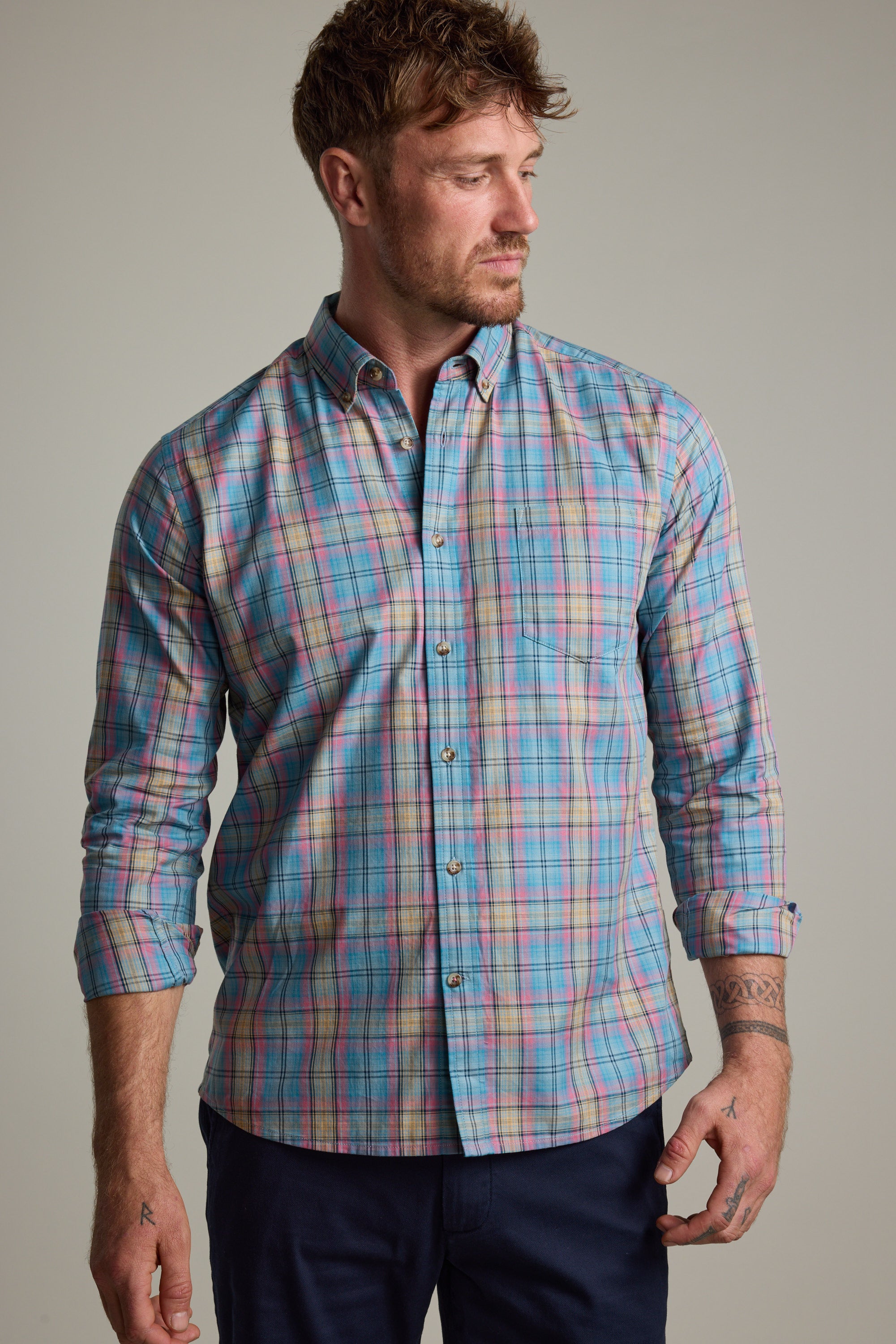 A man in the Barkers Hayne Check Shirt, a lightweight cotton design with rolled-up sleeves and tailored fit, stands against a plain background, glancing left with short, styled hair.