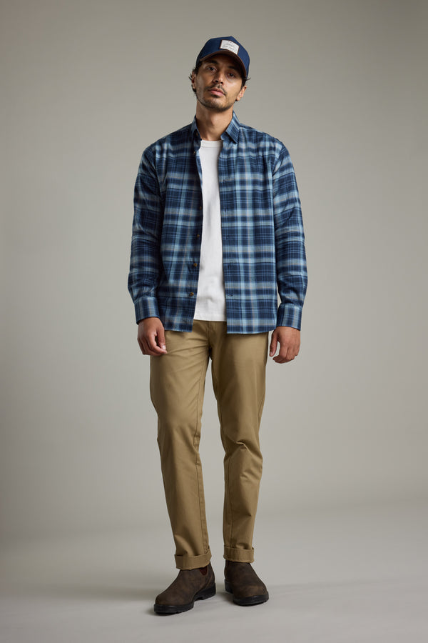 Man in Barkers Lexington Check Shirt, white tee, tan pants, brown boots, and navy cap.
