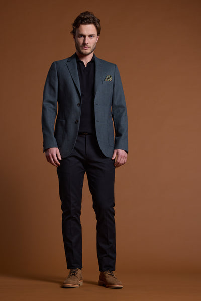 A man with short hair and a neutral expression faces forward against a brown background, wearing the Barkers Yancey Textured Blazer in gray over a black shirt and pants, paired with brown shoes.