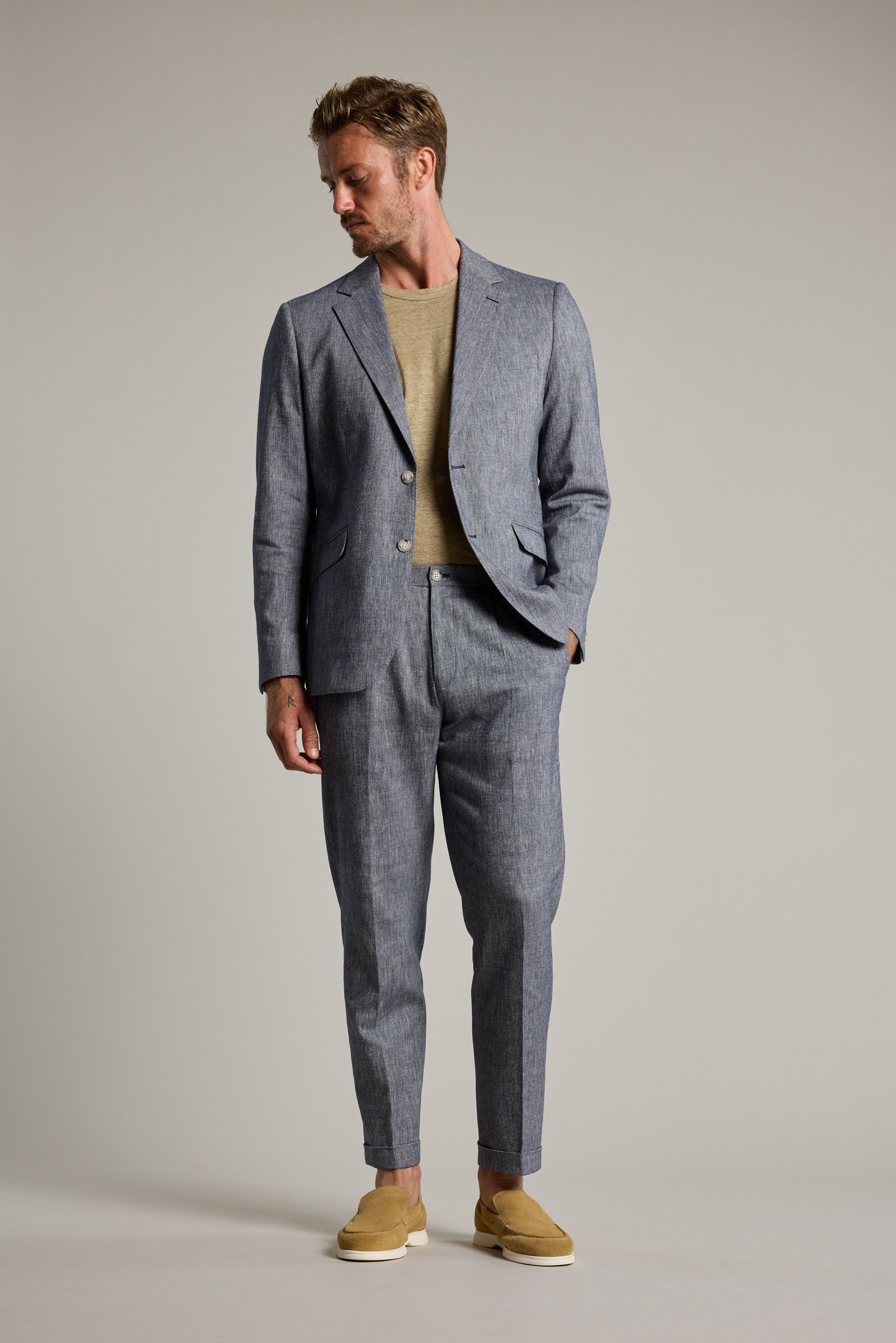 Man wearing Barkers Paden Twill Pant with beige shirt and grey summer suit, looking down.