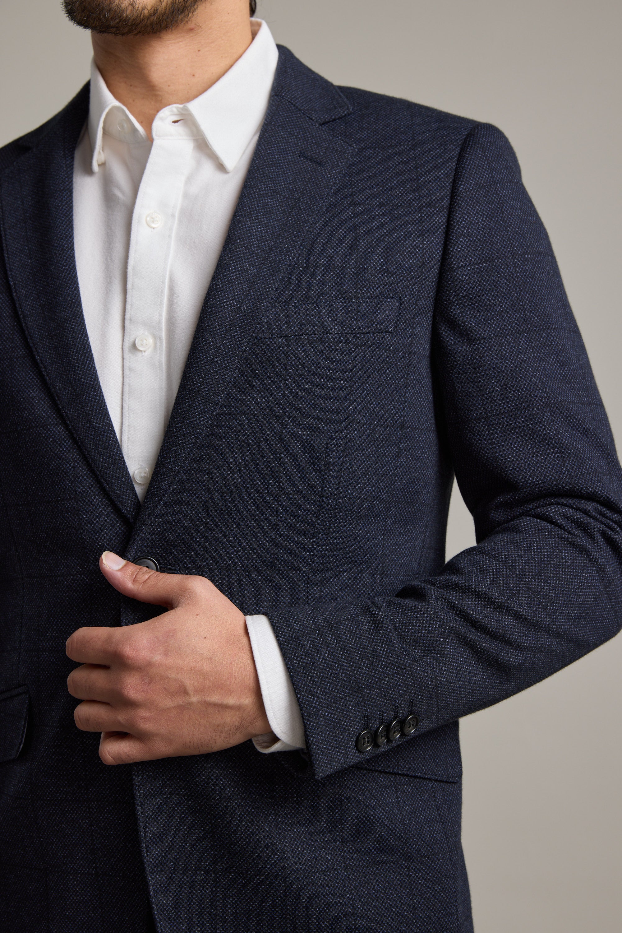 A man wearing a white dress shirt and a Barkers Risca Check Knit Blazer is buttoning his single-breasted blazer. The photo shows his torso and part of his face against a neutral background.