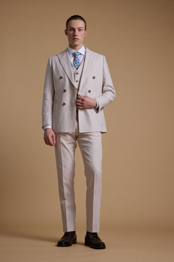 A man faces forward against a beige background wearing the Barkers Somerton Linen Double Breasted Blazer and matching vest, styled with a white shirt, blue patterned tie, and dark brown dress shoes—a perfect summer suit.