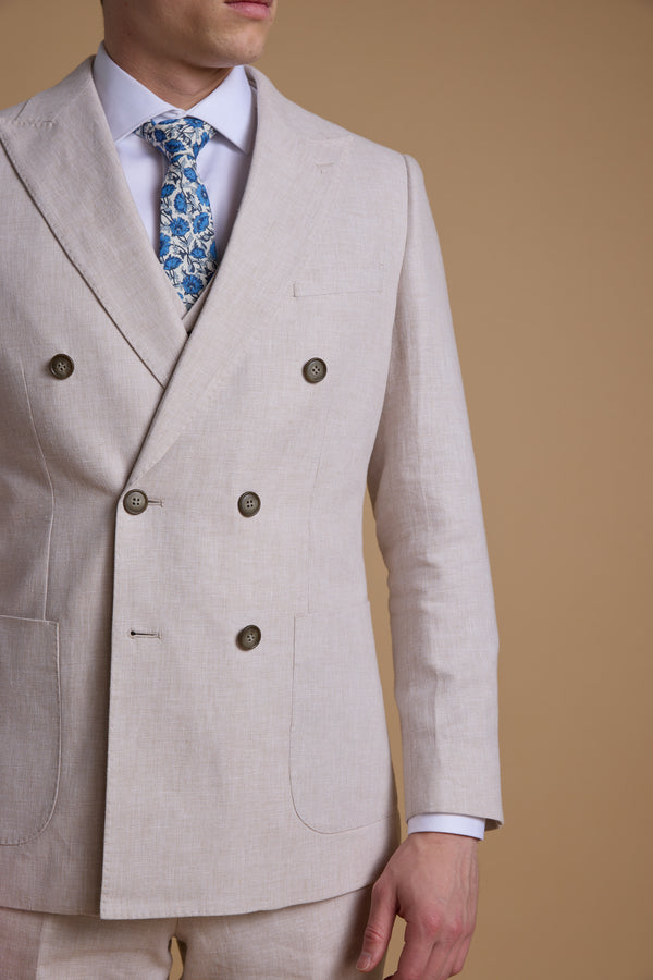 A man wears the Barkers Somerton Linen Double Breasted Blazer with a white shirt and blue floral tie, standing against a plain tan background. His face is partially out of frame.
