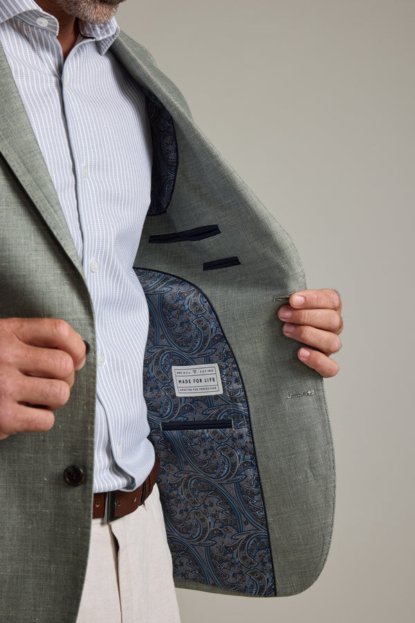 A man opens his Barkers Marion Texture Blazer to reveal a blue paisley lining and a Made for Life label. He pairs it with a striped shirt, light trousers, and a brown belt—an effortless summer look. His face is not shown.