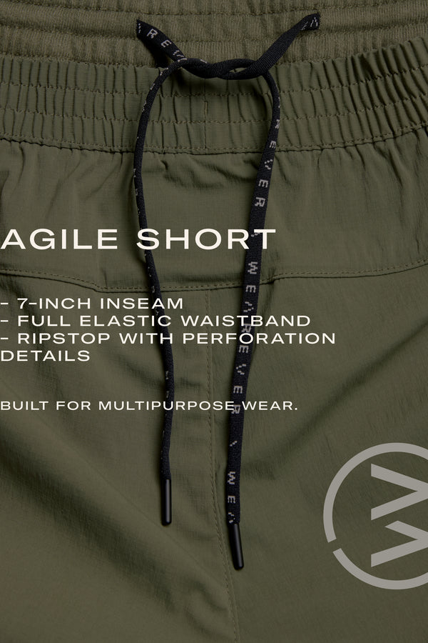 Close-up of WearEver Agile Short in olive green with black drawstrings. White text highlights: 7-inch inseam, full elastic waistband, ripstop with perforation—lightweight, multipurpose stretch shorts by WearEver.