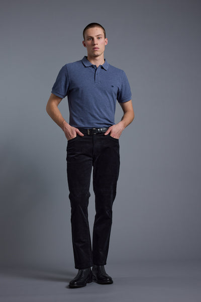 A young man stands against a plain gray background, wearing a Barkers Regent Pique Polo in blue, paired with black pants, a black belt, and black shoes. He has his hands in his pockets and maintains a neutral expression.