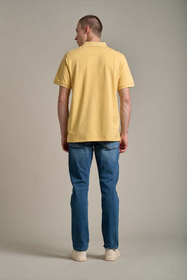 A man stands with his back to the camera, wearing a yellow Barkers Regent Pique Polo, blue jeans, and cream shoes against a plain light gray background.
