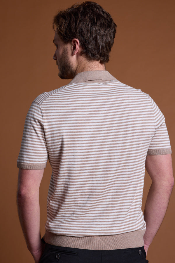 A man stands with his back to the camera, wearing the Barkers Parkway Cotton Stripe Polo in light beige and white stripes with black pants, set against a plain brown background.