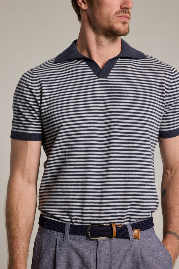 A man wears the Barkers Parkway Cotton Stripe Polo, a short-sleeved navy and white knit shirt with a dark collar, paired with grey-blue trousers and a dark belt. The image is cropped at the shoulders and mid-thigh.