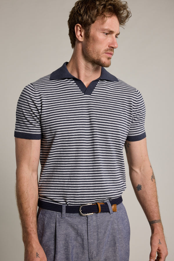 A man with short, wavy hair and facial hair models the Barkers Parkway Cotton Stripe Polo in navy and white, paired with light blue trousers and a navy woven belt. He looks left against a plain background, highlighting the lightweight polo shirt.