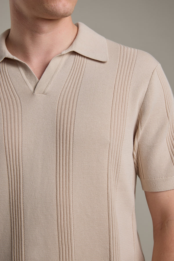A close-up of a person wearing the Barkers Milwood Knit Polo in beige, featuring short sleeves and a textured vertical stripe pattern. The face is partially out of frame against a plain, neutral background—a classic summer essential.