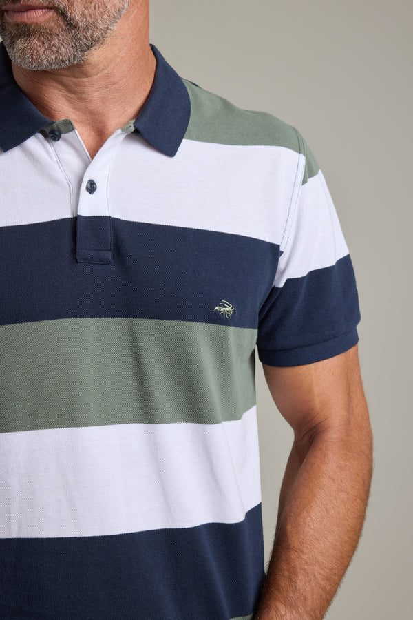 A man wears a Barkers Regent Pique Stripe Polo, a limited edition with short sleeves, wide white, green, and navy stripes, a collar, buttons, and an embroidered chest logo. The polo is partially out of frame.