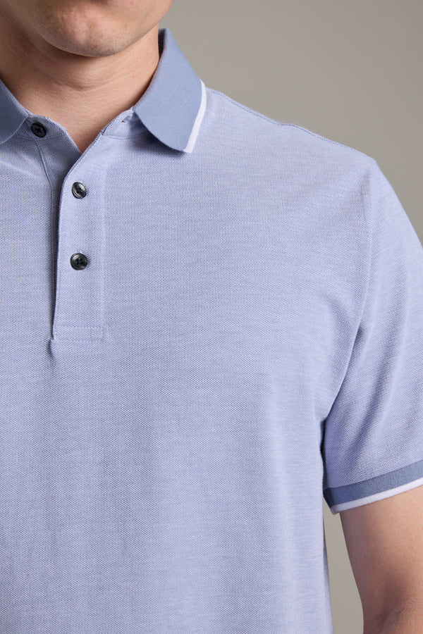 A person is shown wearing the Barkers Birdie Pique Polo in light blue, featuring a collar and three buttons. Only their lower face, neck, shoulders, and upper torso are visible.