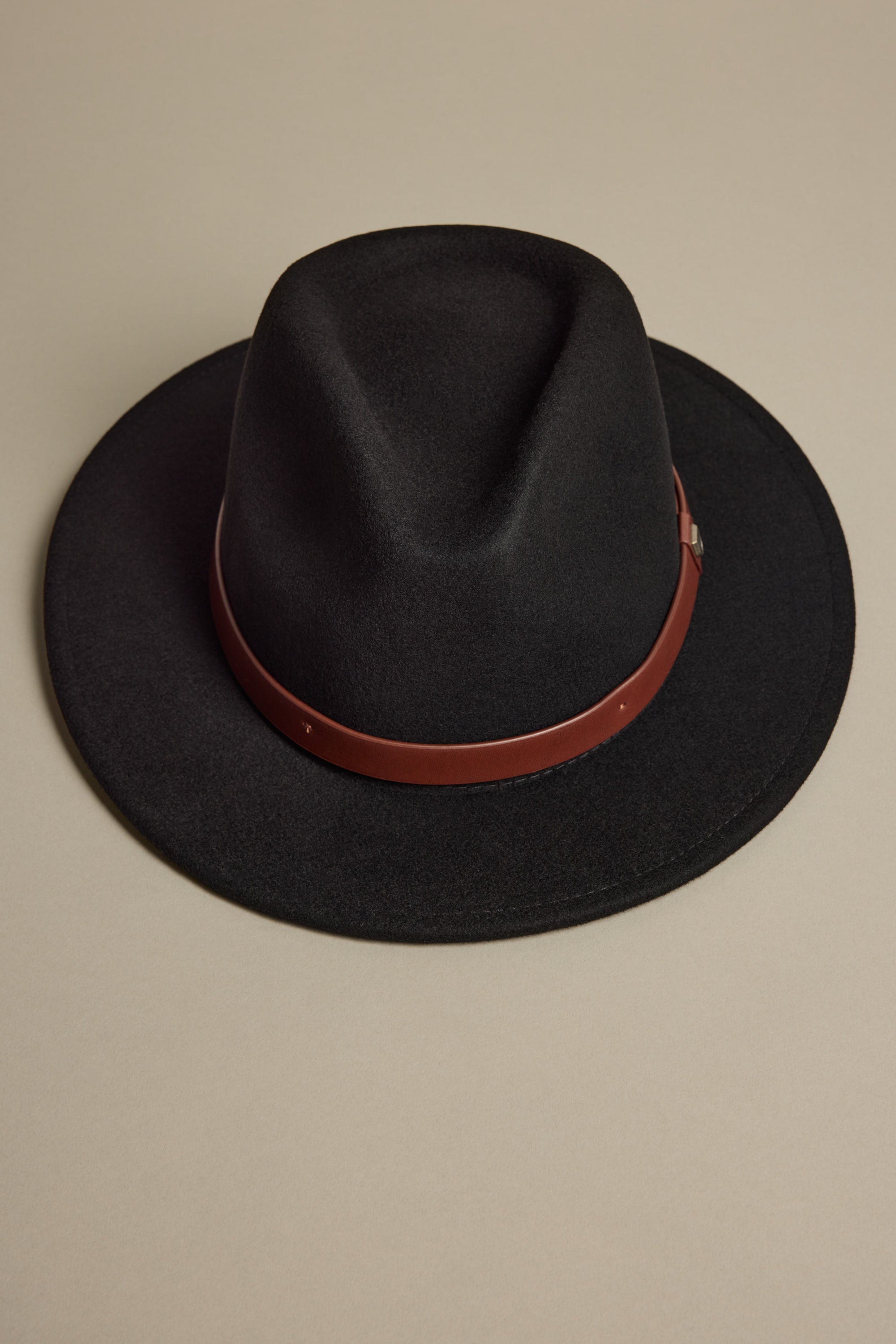 The Brixton Messer Fedora Hat by Brixton is a black wool felt hat with a wide brim, brown leather band, and adjustable strap, shown on a beige surface.