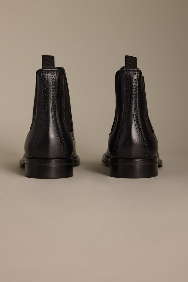 The Barkers Peter Chelsea Boot—a pair of black premium leather boots with brogue detailing—is shown from the back against a plain beige background.