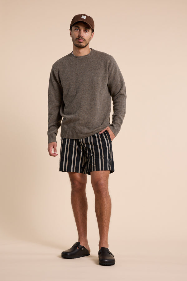 A man stands against a beige background wearing Barkers’ Lawton Stripe Short with an elasticated waistband, a brown sweater, black slip-on shoes, and a brown cap. He has one hand in his pocket and looks at the camera neutrally.