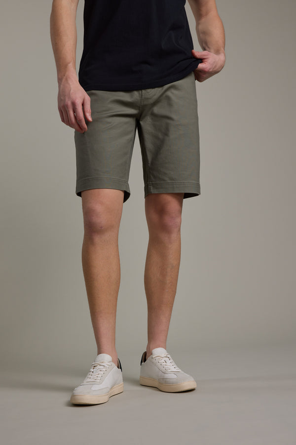 A person wears Barkers Anvil 5Pkt Short in olive green with an elasticated waistband, paired with a black T-shirt and white sneakers. The image, cropped from shoulders down, features a plain light background.