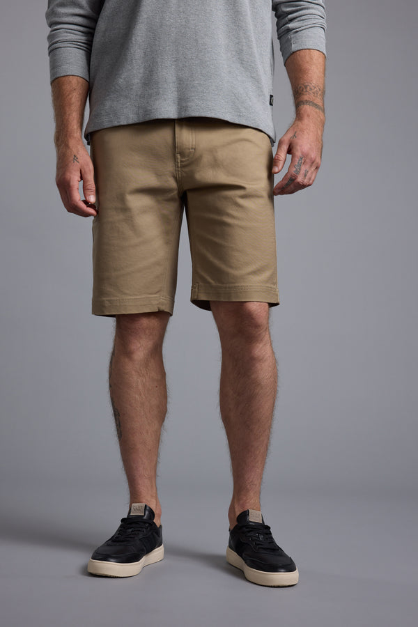 A person, visible from chest to feet, wears a light gray long-sleeve shirt, Barkers Anvil 5Pkt Short with an elasticated waistband, and black sneakers with white soles against a plain gray background.