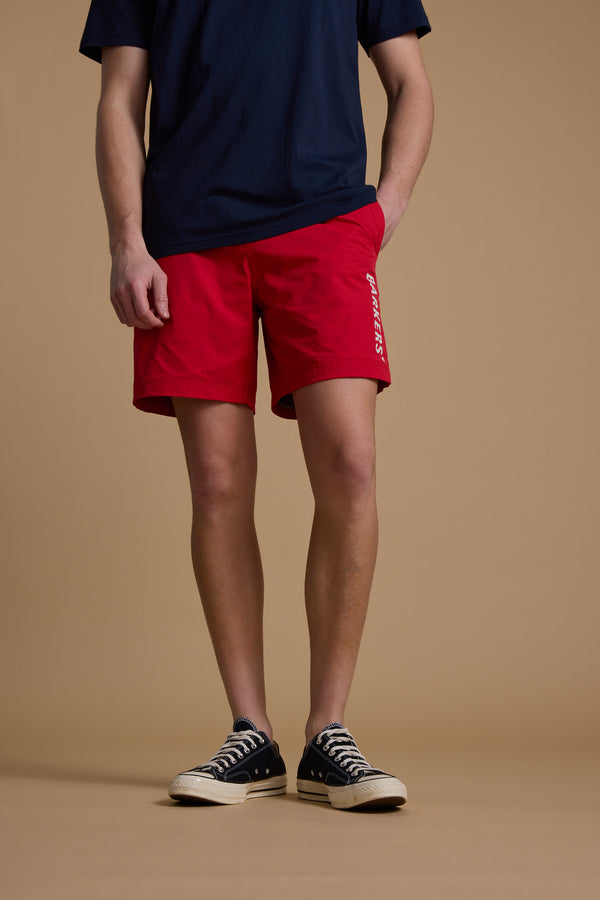 A person stands against a beige background wearing a navy t-shirt, Barkers Weekend Shorts, and black-and-white sneakers. Their left hand is in their pocket. The photo is cropped at the shoulders.