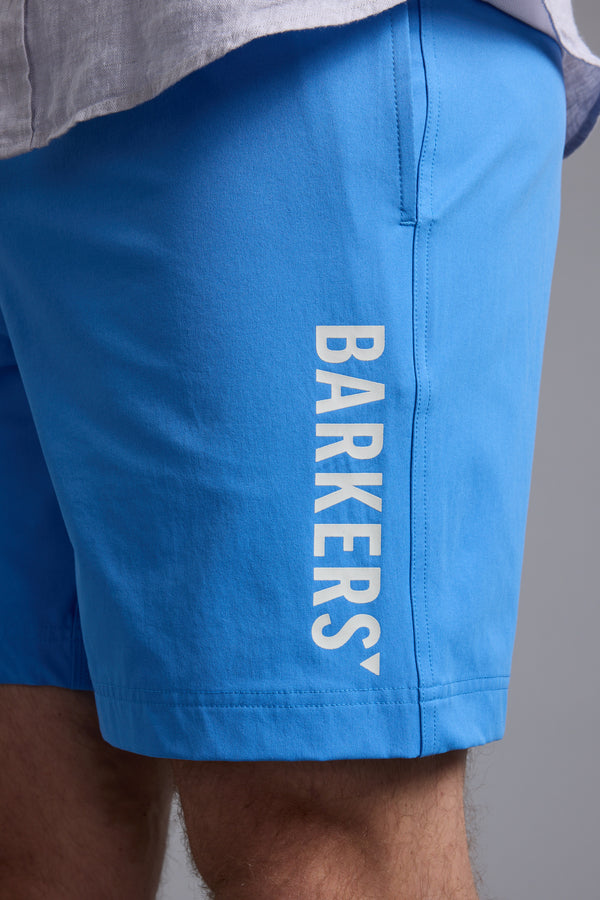 Close-up of a person wearing bright blue Barkers Weekend Shorts, featuring "BARKERS" printed vertically in white on the left leg. The shorts are made from recycled polyester, with part of a light shirt visible at the top.