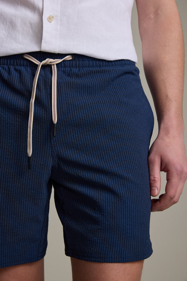 A person wearing a white button-up shirt and Barkers Dehaven Stripe Volley shorts, one arm at their side. The image is cropped from shoulders to mid-thigh.