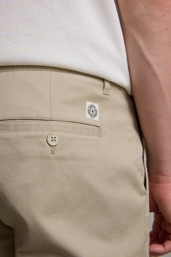 Close-up of a person wearing Barkers Braddock Walk Short in beige and a white shirt, highlighting the back pocket with a button and small white logo label above it—a versatile staple for any wardrobe.