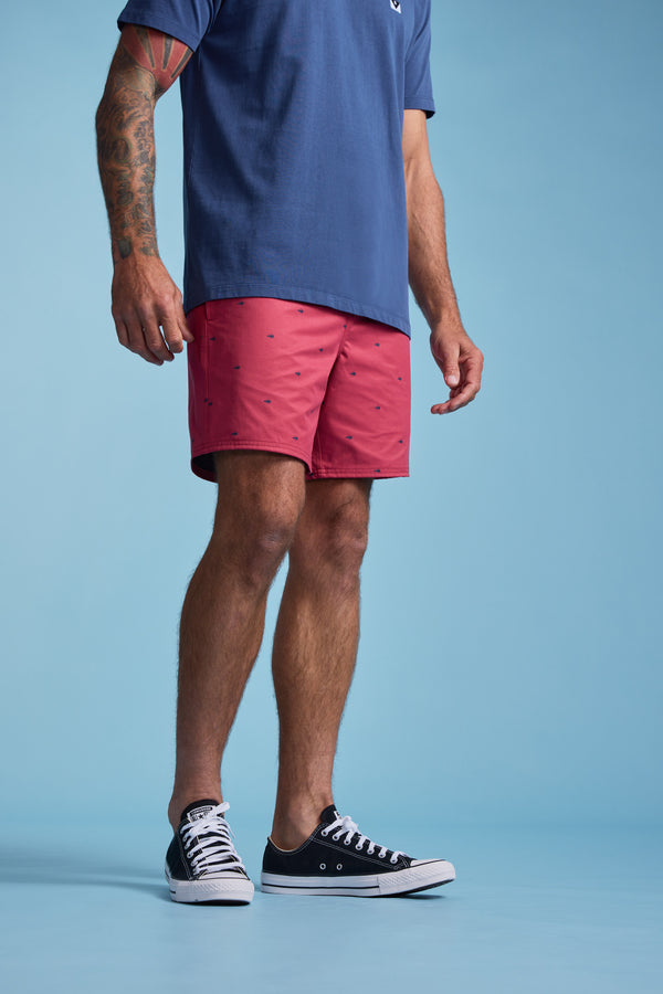 Wearing Barkers Crayfish Print Volley shorts made from recycled polyester, a tattooed person stands against a plain light blue background. The photo is cropped below the shoulders.