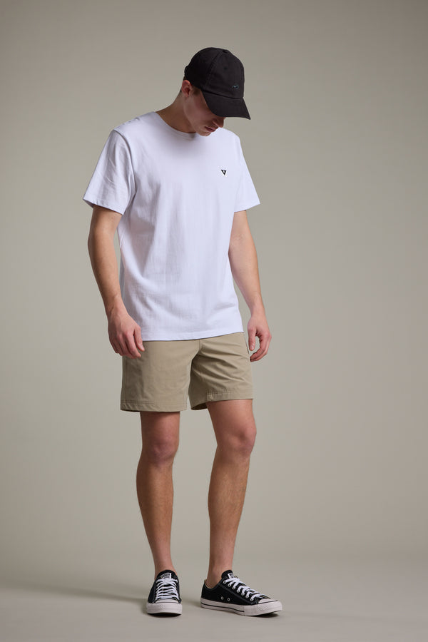 A person in a black cap, white t-shirt, Barkers Davis Weekend Short in khaki, and black sneakers stands against a plain light gray background, looking downward with hands by their sides.