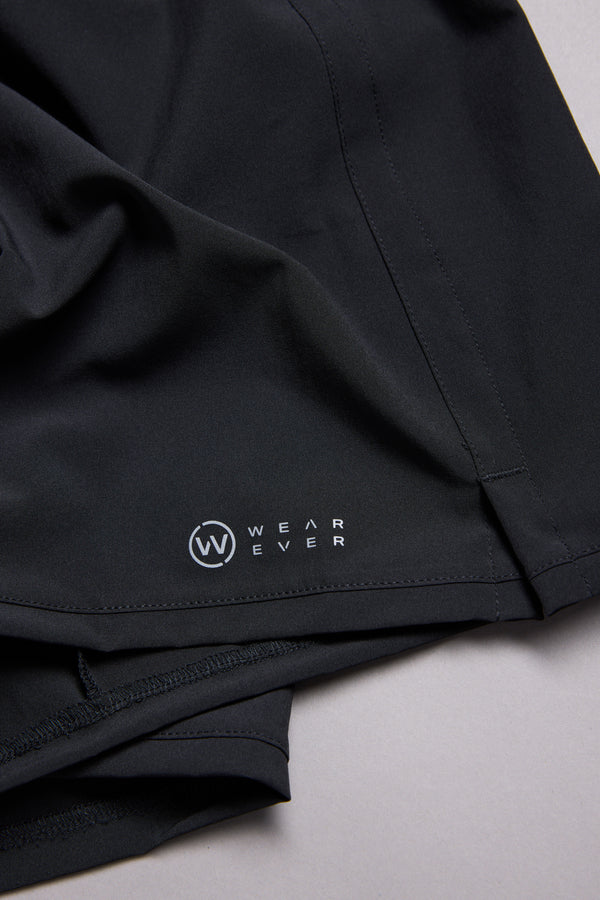Close-up of black WearEver Cadence Shorts, featuring a 5-inch inseam and the white WearEver logo near the hem, laid flat on a light gray surface.