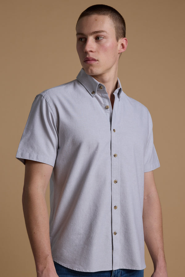 A person wearing the Barkers Archer Oxford Shirt in light gray with a button-down collar stands against a plain beige background, looking slightly to the side.