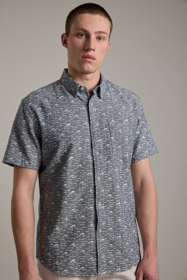 A young man with short hair wears the Barkers Shelby Print Shirt, a short-sleeve summer shirt crafted from responsibly sourced cotton, standing against a plain, light-colored background.